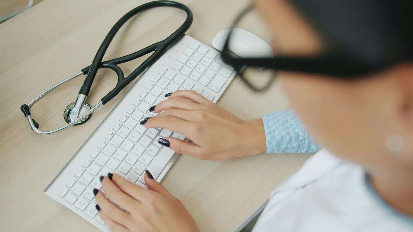 Clinician typing on a keyboard beside a stethoscope