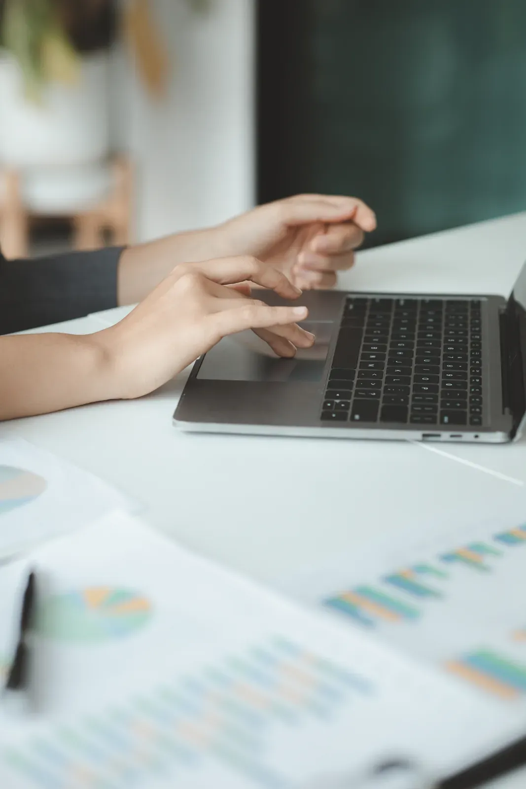 Hands on a laptop at a white desk with printed charts